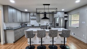 A modern kitchen with grey cabinets, a central island with bar stools, stainless steel appliances, and a window with a view.