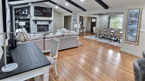 A spacious living room with a fireplace, a dining area with a table and chairs, and a kitchen area with a stove.