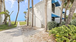 A modern building with a white facade and blue accents, surrounded by palm trees and a pathway leading to the beach. - Studio by the Sea | Beach, Pool & Sunset Vibes (Longboat Key)