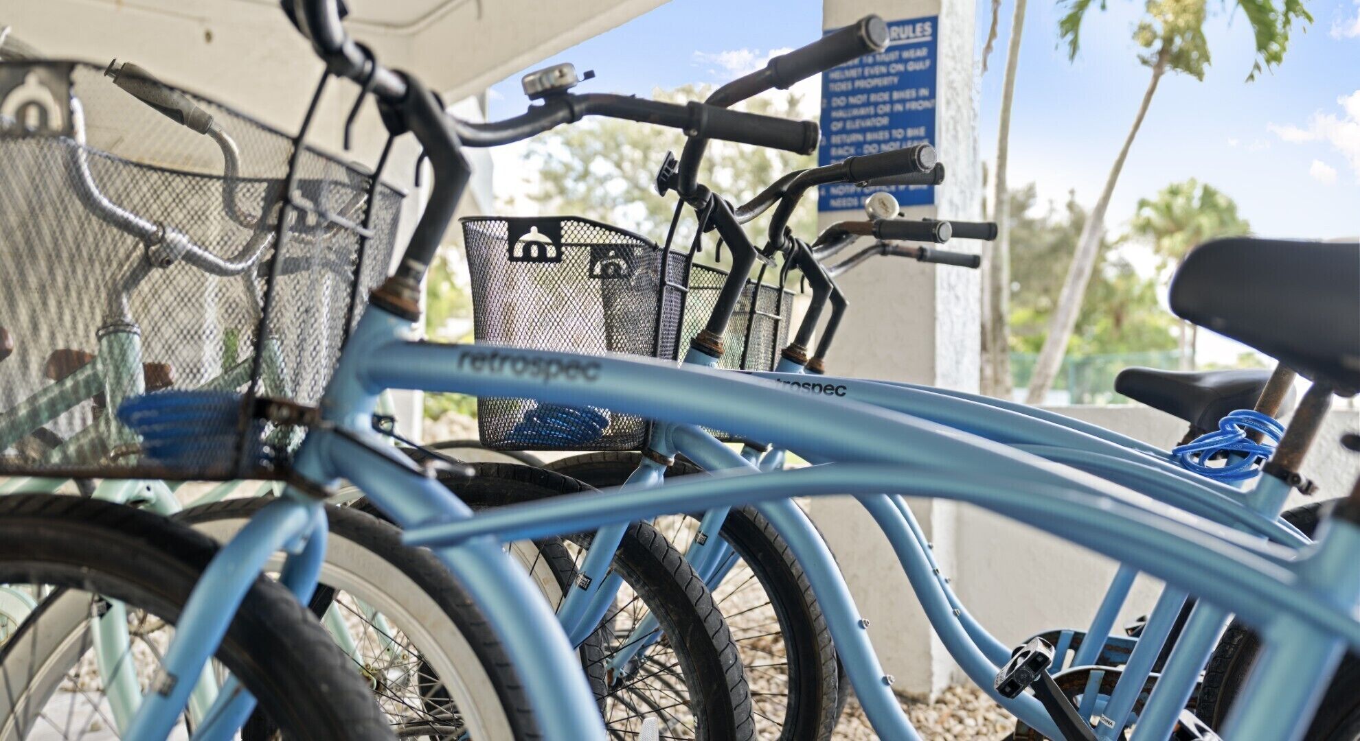 A blue bicycle with a basket and a rear rack, parked near a sign with rules.