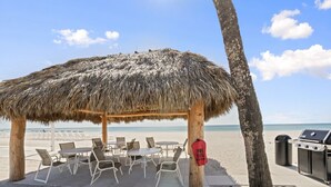 A beachside gazebo with a thatched roof, surrounded by white metal chairs and tables. - Bayside Comfort | 2BR Condo with Beach Access & Resort Amenities (Longboat Key)