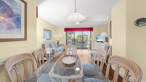 A spacious living area with a dining table, wicker chairs, a sofa, and a TV. - Bayside Comfort | 2BR Condo with Beach Access & Resort Amenities (Longboat Key)