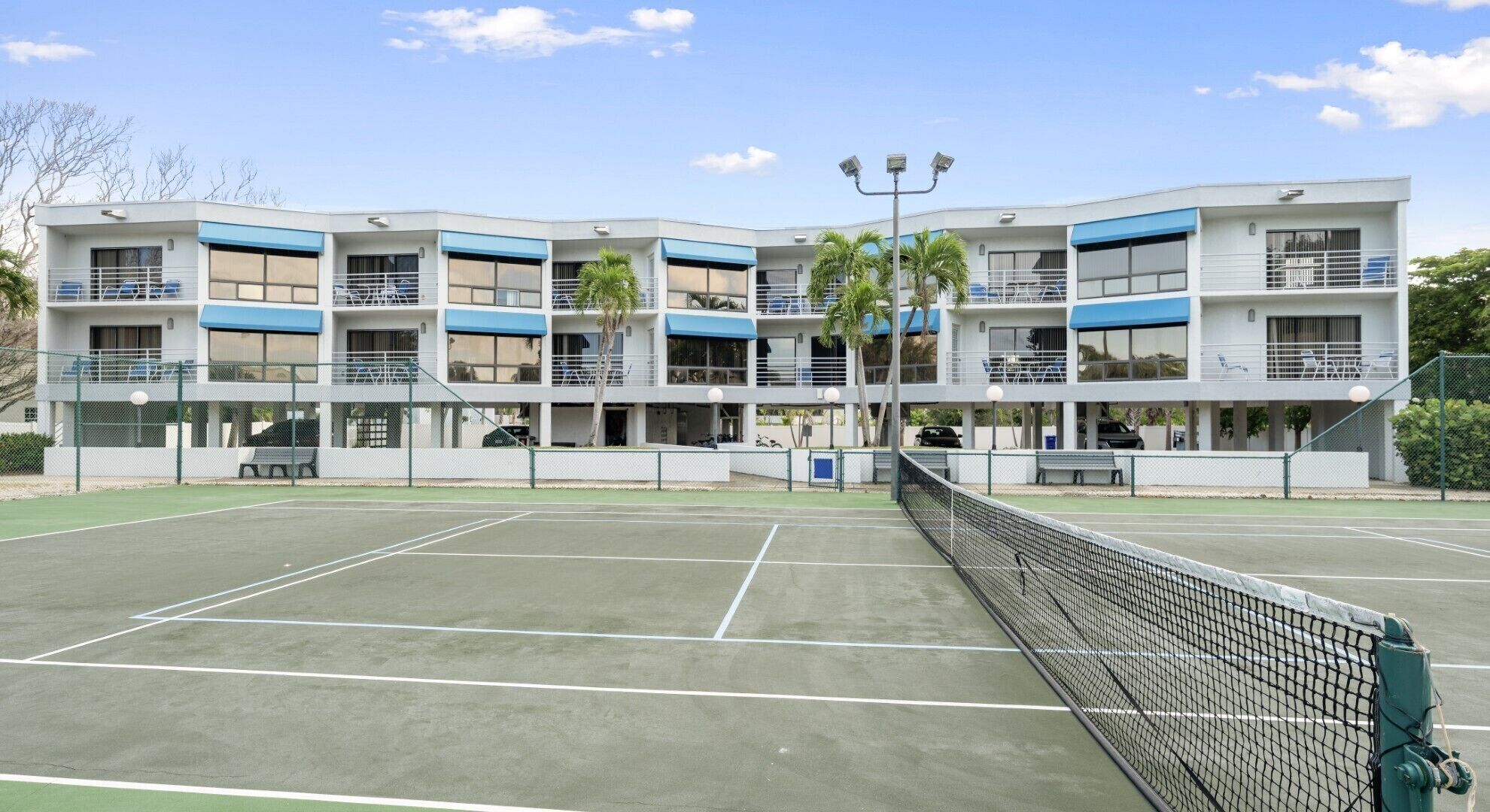 A multi-story building with balconies, a tennis court, and a fence.