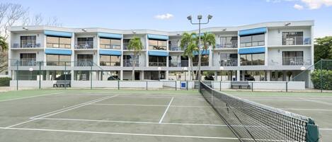 A multi-story building with balconies, a tennis court, and a fence.