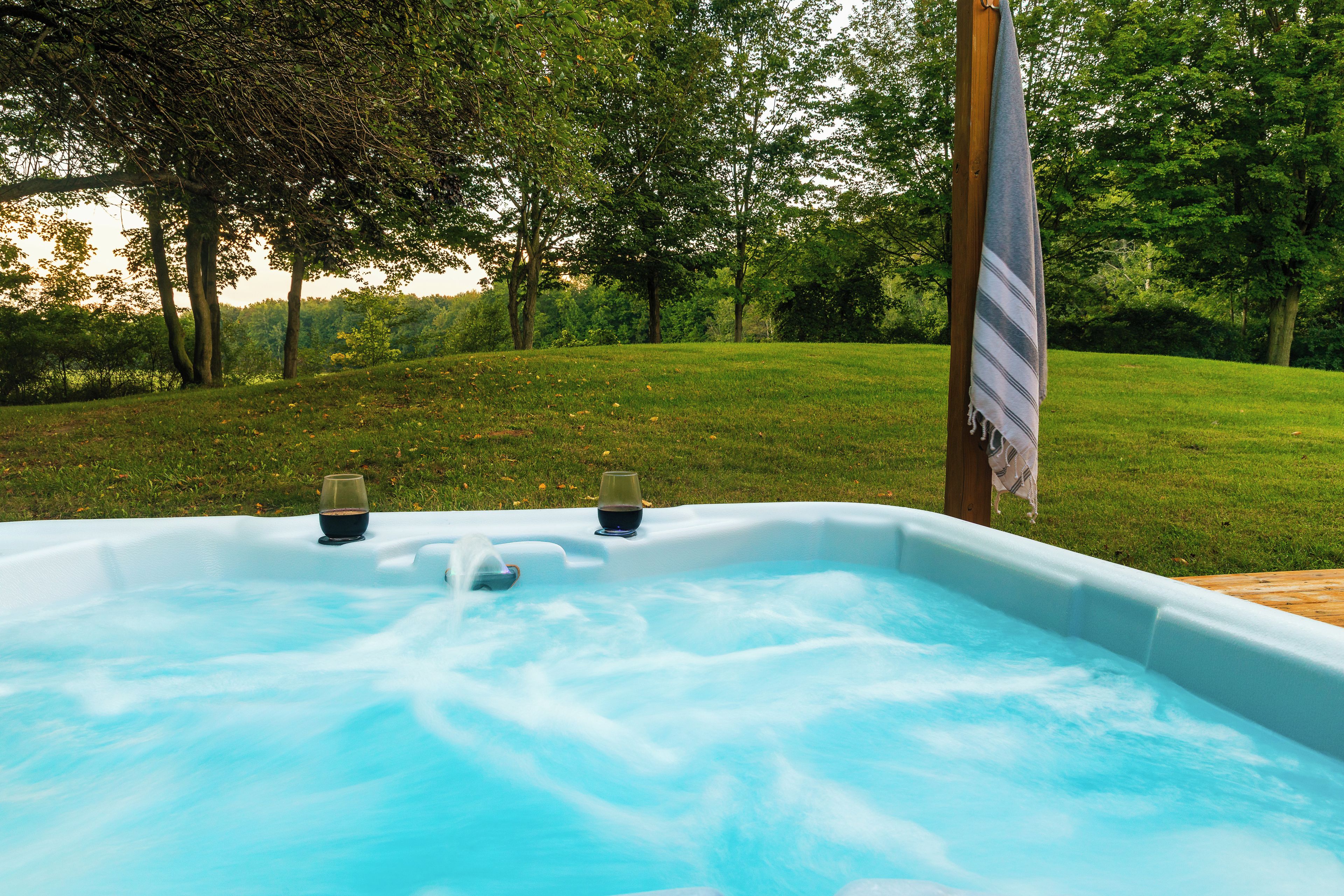 Un jacuzzi en un área exterior con césped y árboles al fondo.