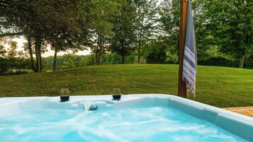 Un jacuzzi en un área exterior con césped y árboles al fondo.