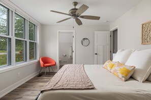 Un dormitorio con una cama, ventilador de techo, ventana y puerta.