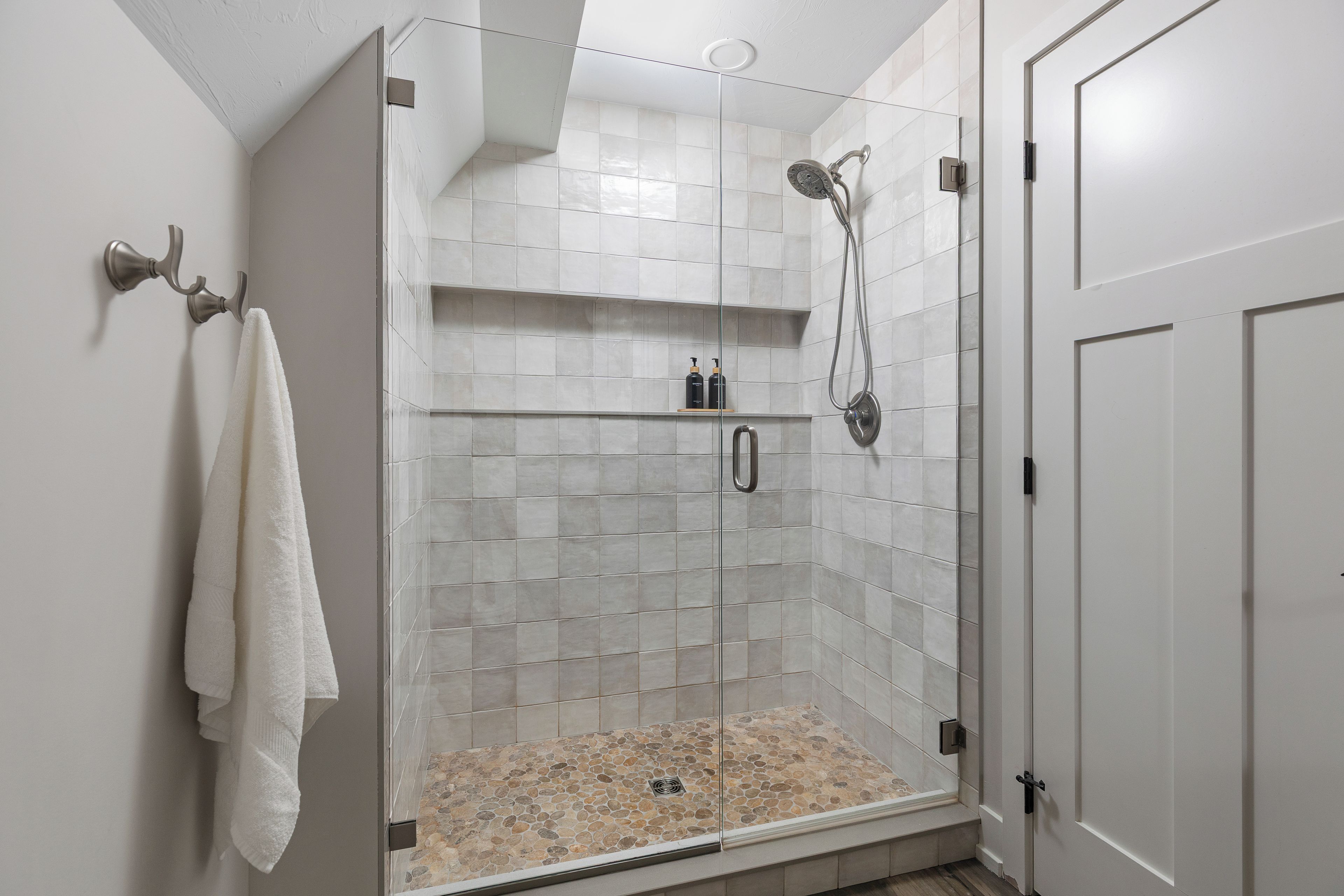 Una ducha a ras de suelo con puerta de cristal, paredes de azulejos y un cabezal de ducha.