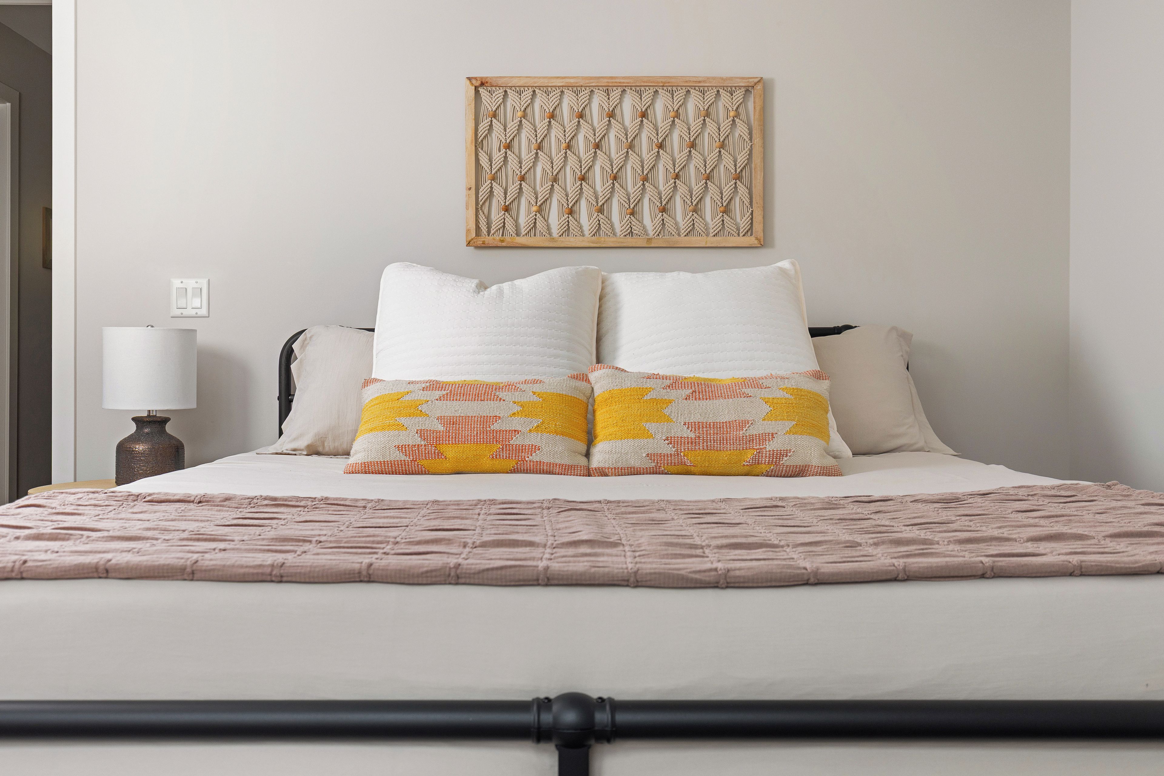 Un lit bien fait, avec une couvre-lit à motifs, deux oreillers et une décoration en macramé accrochée au mur.
