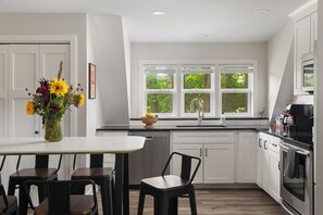 A modern kitchen with white cabinetry, a dining area with a table and chairs, and a window with a view of greenery.