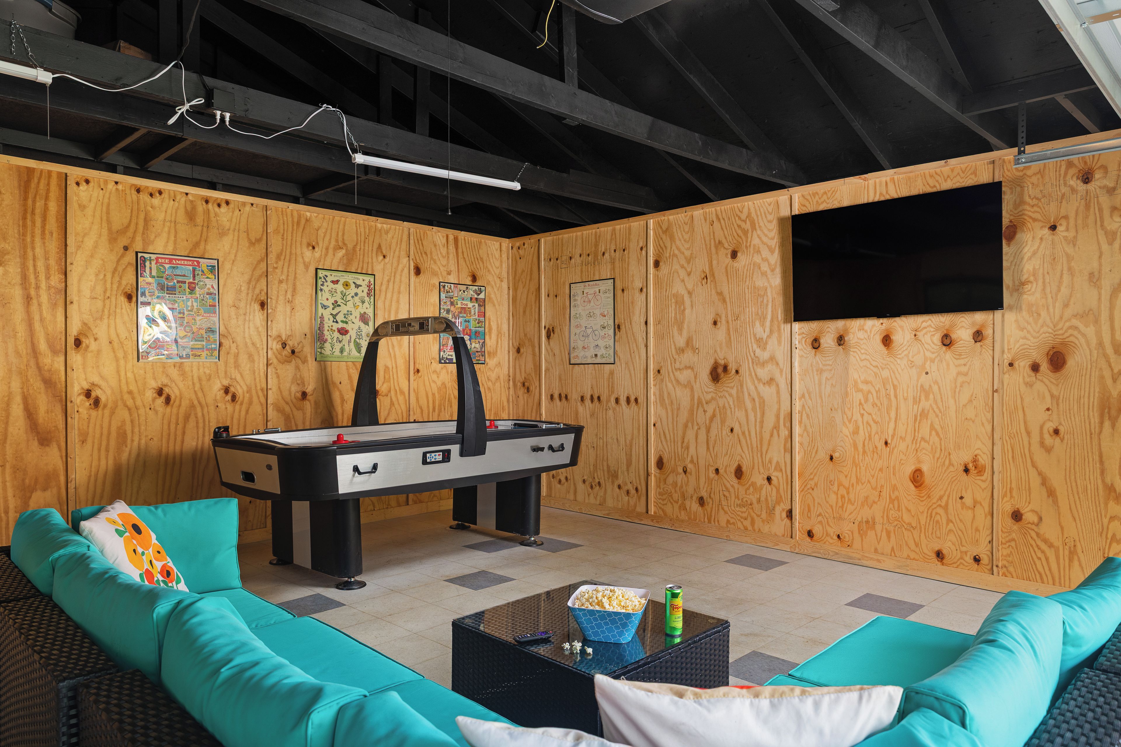 A room with a pool table, teal sofa, and a television mounted on the wall.