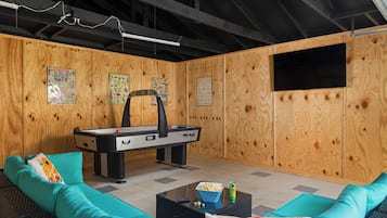A room with a pool table, teal sofa, and a television mounted on the wall.