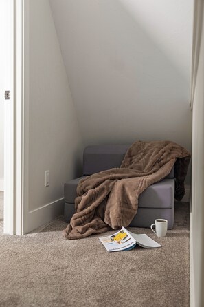 A room with a grey sofa, a brown blanket, a white mug, and a magazine on the floor.