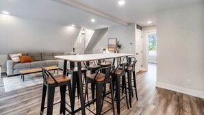 A modern interior with a dining area featuring a white table and black chairs, a grey sofa with orange cushions, and a wooden floor. - Applewood Lodge: Private A-Frame with Hot Tub Near Saugatuck & Lake Michigan (Fennville)