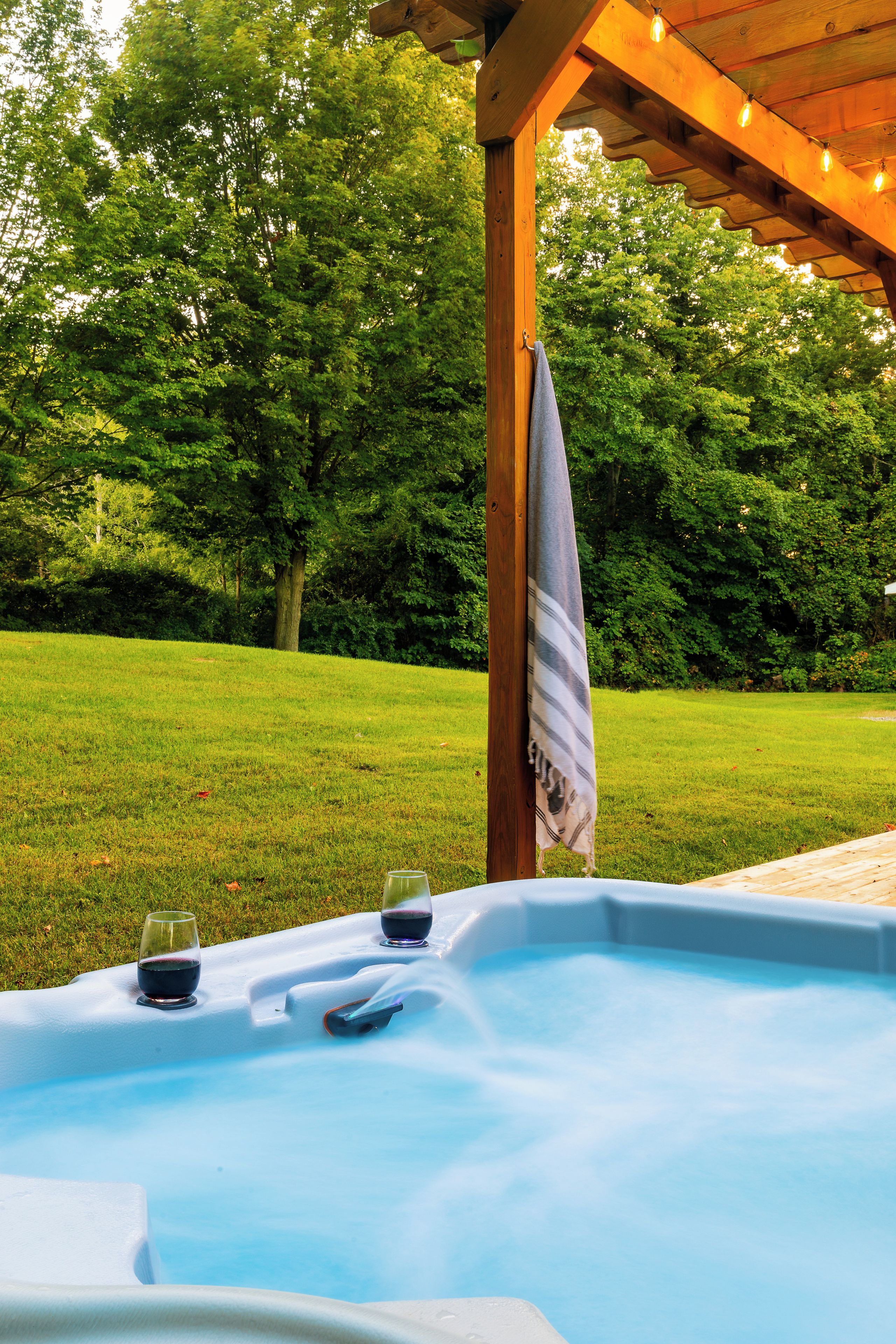 A hot tub with a tablecloth, two glasses of wine, and a towel hanging on a wooden structure.