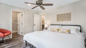A bedroom with a bed, a ceiling fan, a red chair, and a wall-mounted artwork. - Applewood Lodge: Private A-Frame with Hot Tub Near Saugatuck & Lake Michigan (Fennville)