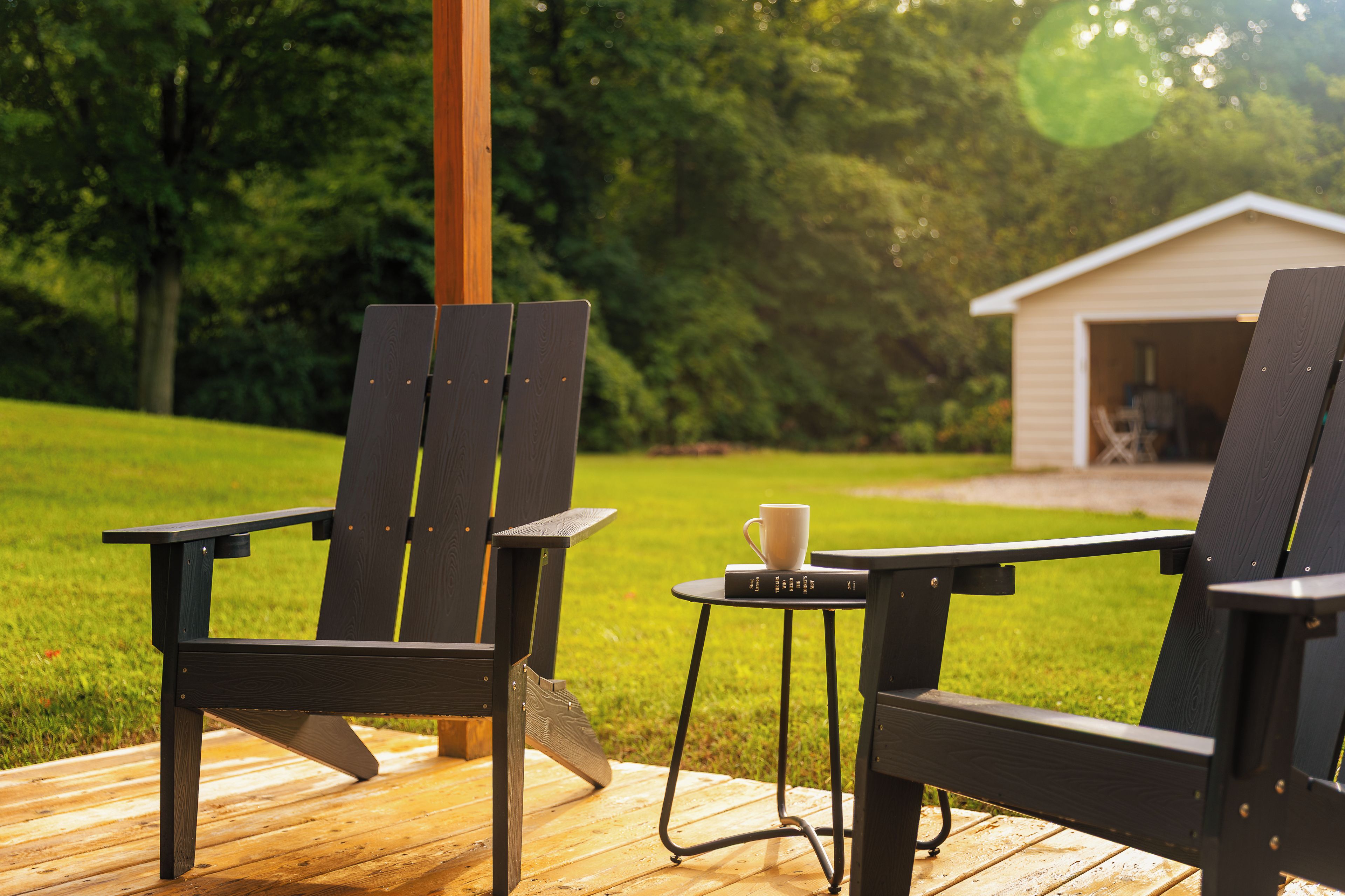 Zwei Adirondack-Stühle auf einer Holzterrasse, dazwischen ein kleiner Tisch und eine Kaffeetasse.