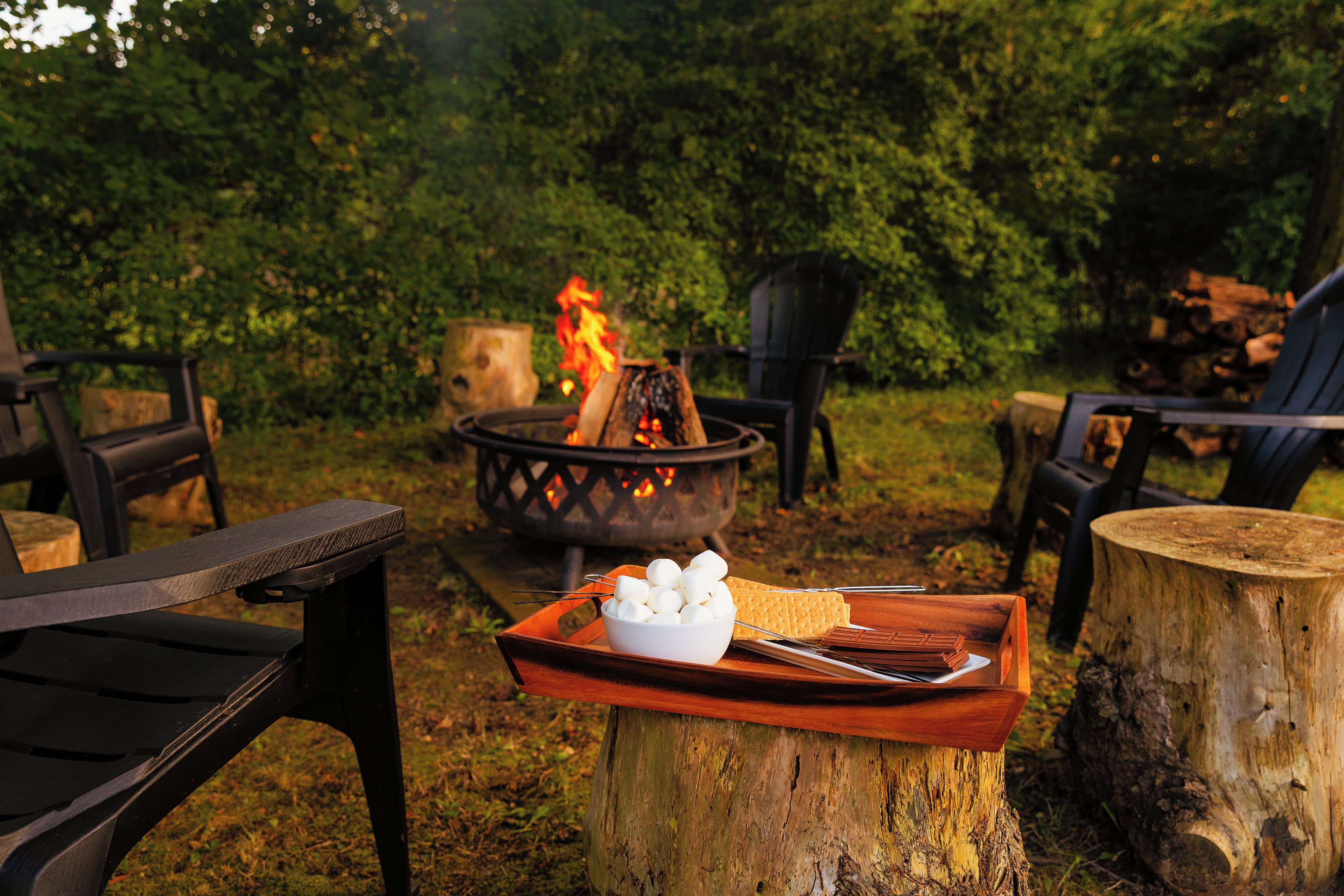 An outdoor seating area with a fire pit, chairs, and a table with marshmallows and chocolate.
