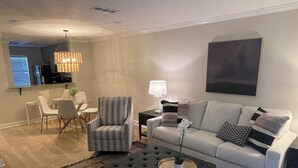 A modern living room with a sofa, armchair, and ottoman. There is a dining area with chairs and a table. A lamp and a plant are on a side table. - Newly renovated!! Walk to Campus, Swayze and the Square (Oxford)