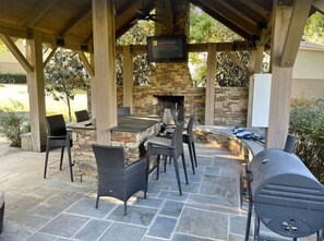 Une terrasse extérieure avec un sol en pierre, une cheminée en pierre et un espace barbecue.