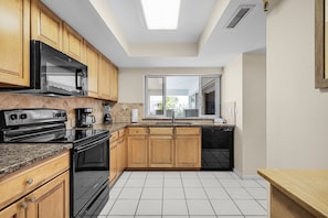 A modern kitchen with wooden cabinets, a black stove, and a window overlooking a balcony.