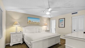 Une chambre à coucher avec un lit, deux tables de chevet avec des lampes, un ventilateur de plafond et un tableau au mur.