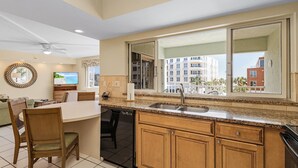 A modern kitchen with a built-in dishwasher, wooden cabinets, and a large window offering a view of the city. - Welcome to your happy place—aka where real life takes a vacation. (Sarasota)