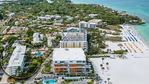 An aerial view of a coastal hotel with multiple buildings, a beach with umbrellas, and a swimming pool. - Welcome to your happy place—aka where real life takes a vacation. (Sarasota)