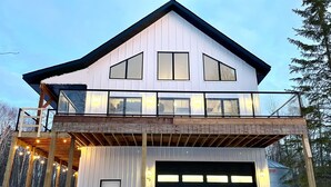 A two-story house with a garage, a balcony with string lights, and a snowy landscape.