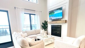 A modern living room with a beige sofa, a white armchair, a glass coffee table, and a fireplace.