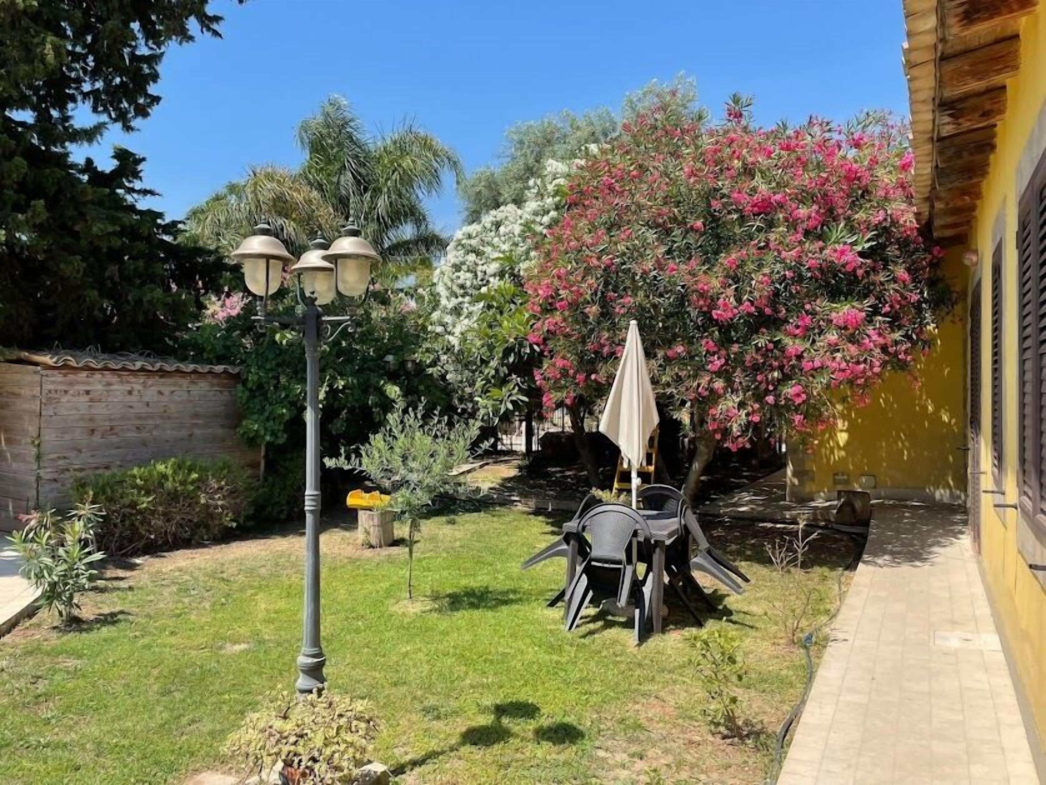 Un jardin avec une table et des chaises, un lampadaire et un arbre aux fleurs roses.