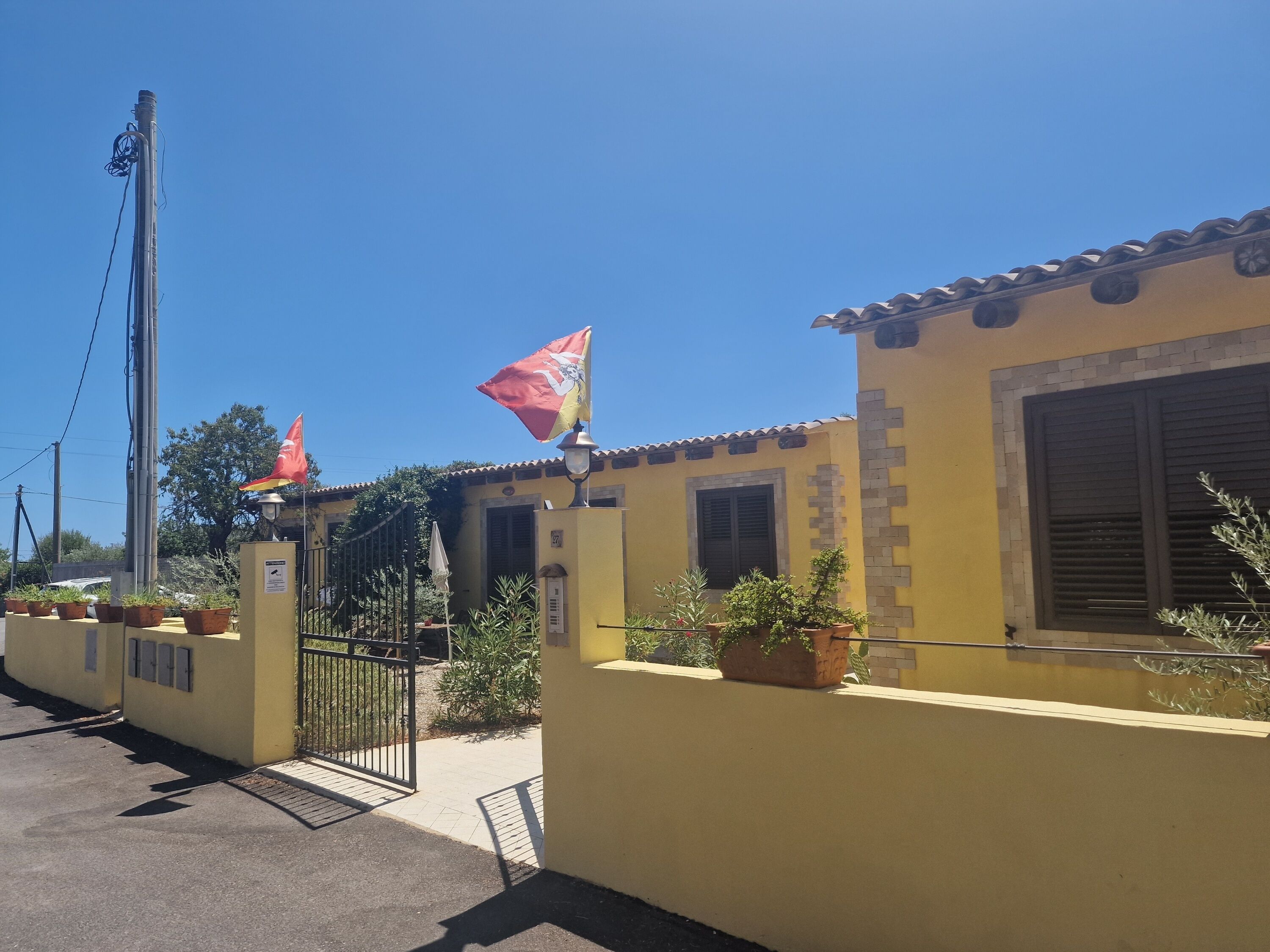Un edificio amarillo con techo de tejas, un portón y plantas en macetas.