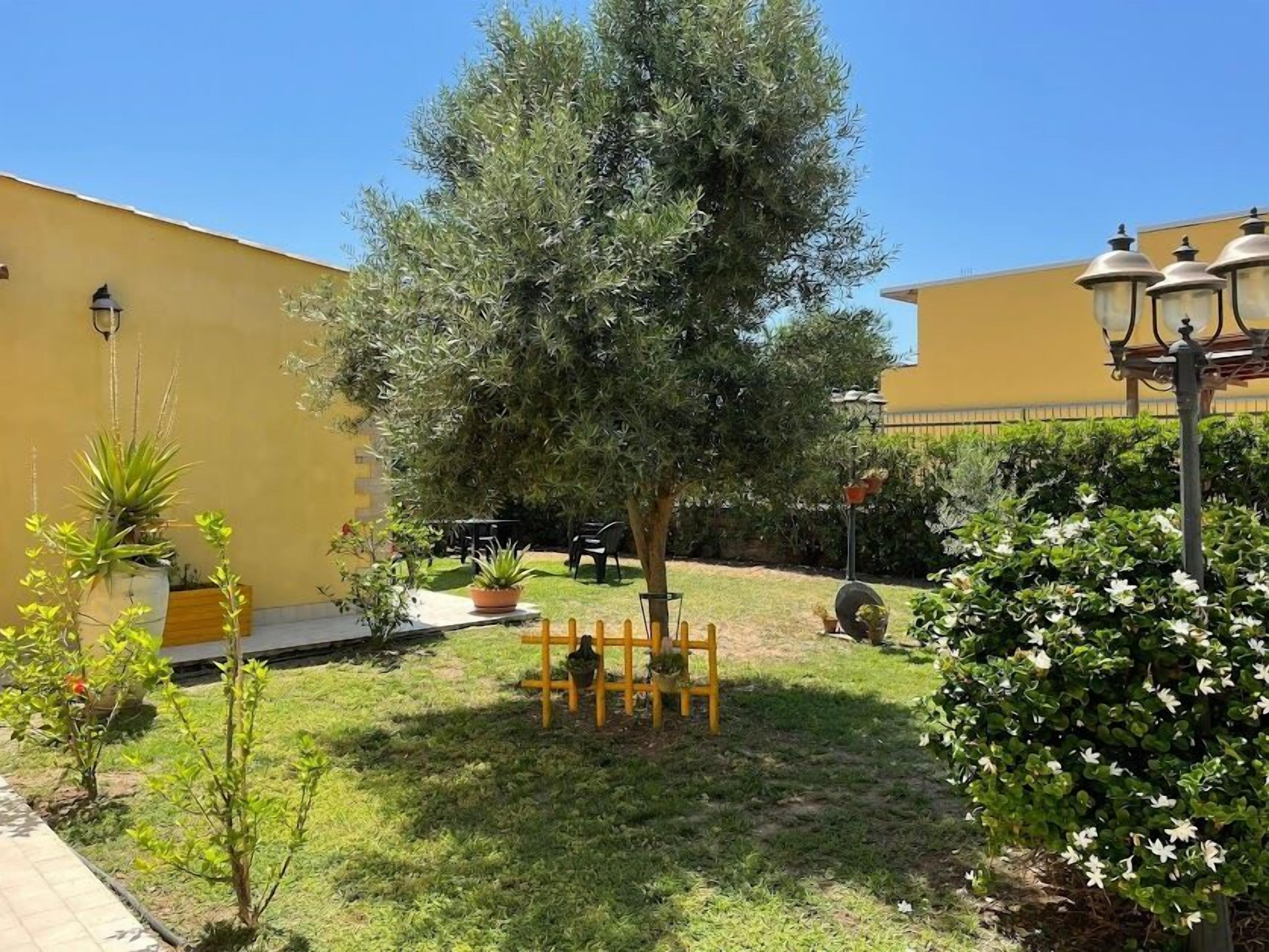 Ein Innenhof mit einem großen Baum, Blumentöpfen, Gartenmöbeln und einem gelben Gebäude.