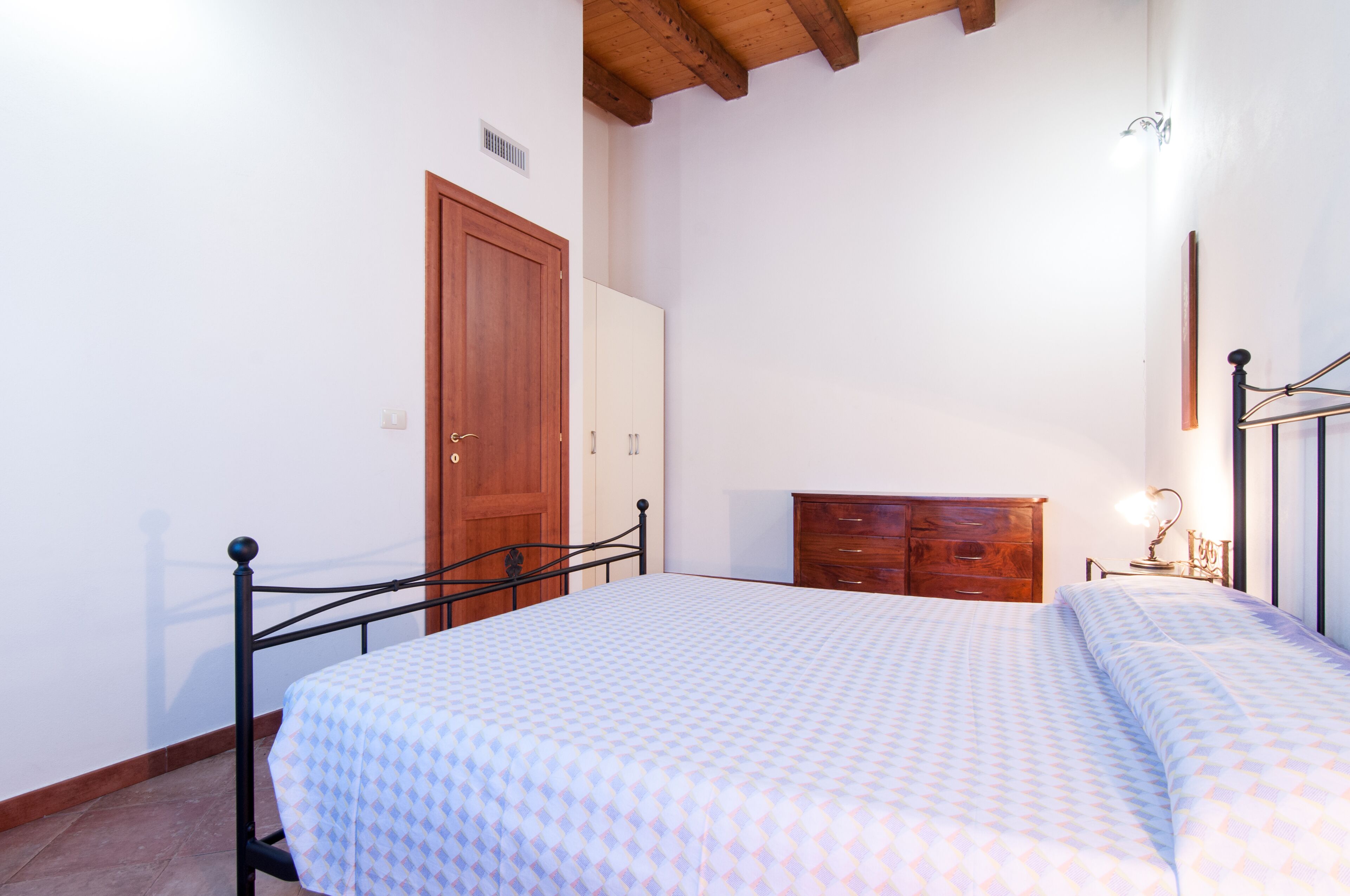 A bedroom with a bed, wooden wardrobe, and a nightstand with a lamp.