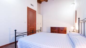 A bedroom with a bed, wooden wardrobe, and a nightstand with a lamp.
