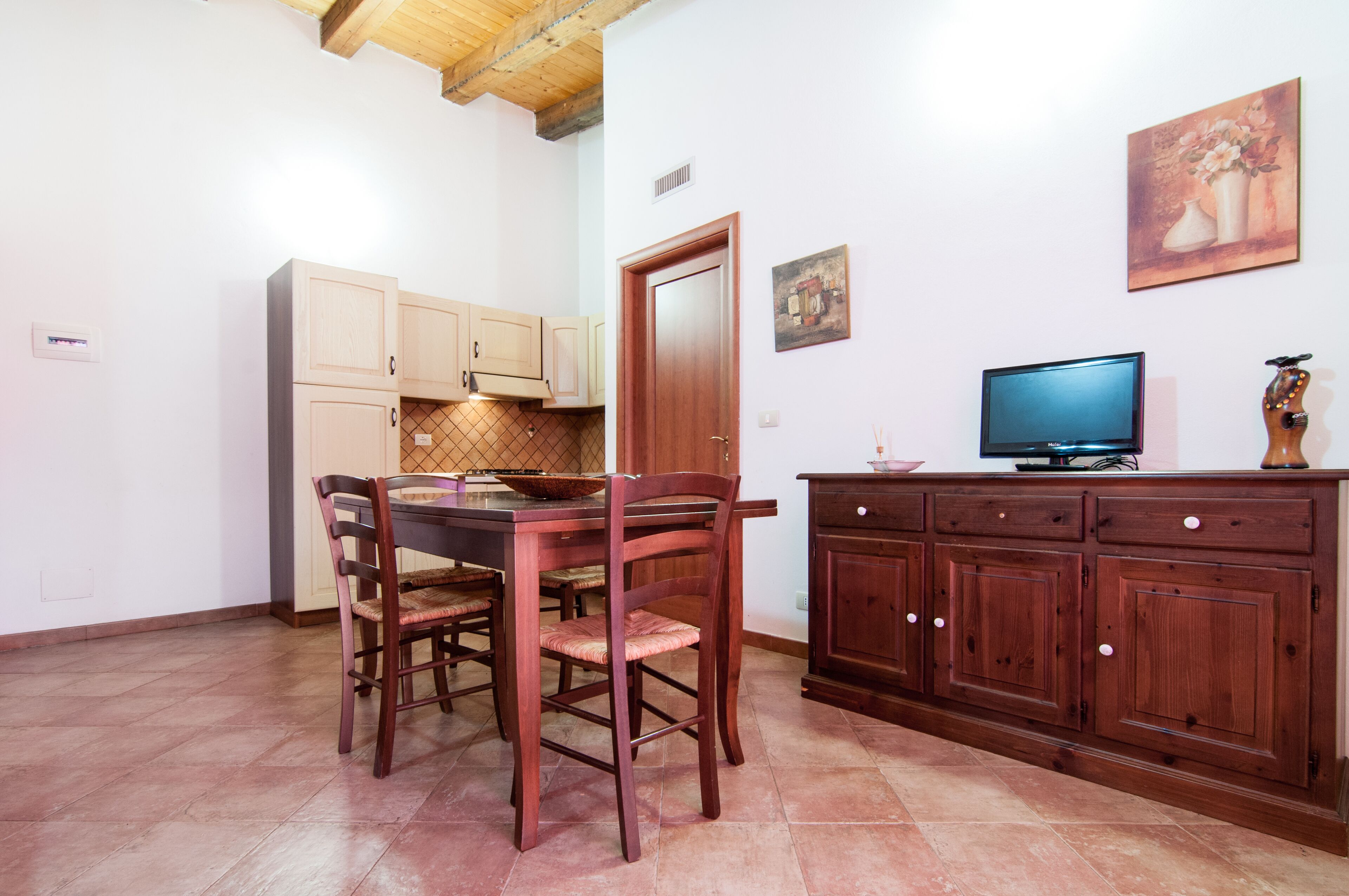 A dining area with a wooden table and chairs, a wooden cabinet, a television, and a painting on the wall.