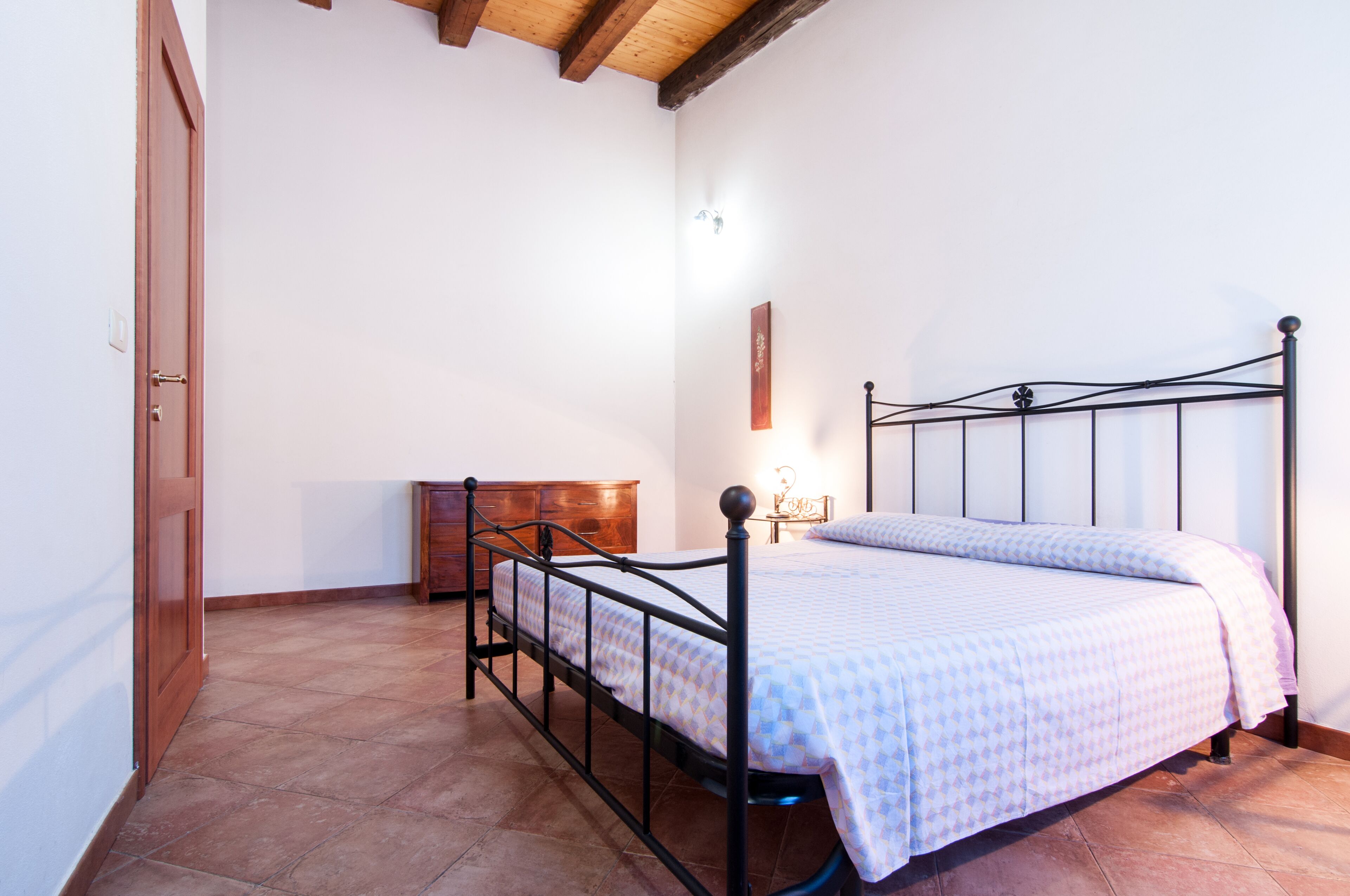A bedroom with a metal bed frame, a wooden dresser, and a tiled floor.