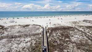 Une plage avec une promenade en bois menant à la rive, des dunes de sable et une vue dégagée sur l’océan.