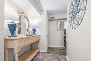 A hallway with a wooden vanity, two blue lamps, a mirror, and a decorative metal piece on the wall. - Incredible Ocean Front Views, Indoor/Outdoor Pool, Hot Tub, Fully Stocked, 4 TVs (Orange Beach)