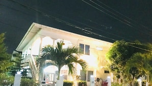 Un immeuble de deux étages avec une façade blanche, un balcon apparent et une entrée fermée par un portail.