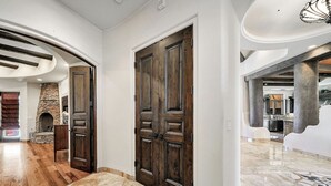 A spacious hallway with a stone fireplace, wooden doors, and a marble floor. - Sonoran Desert Retreat - Quiet, Gated, Custom home with Incredible SUNSETS ! (Scottsdale)