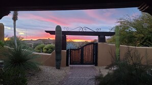 A gated entrance with a wooden gate and a metal archway, surrounded by cacti and desert vegetation. - Sonoran Desert Retreat - Quiet, Gated, Custom home with Incredible SUNSETS ! (Scottsdale)