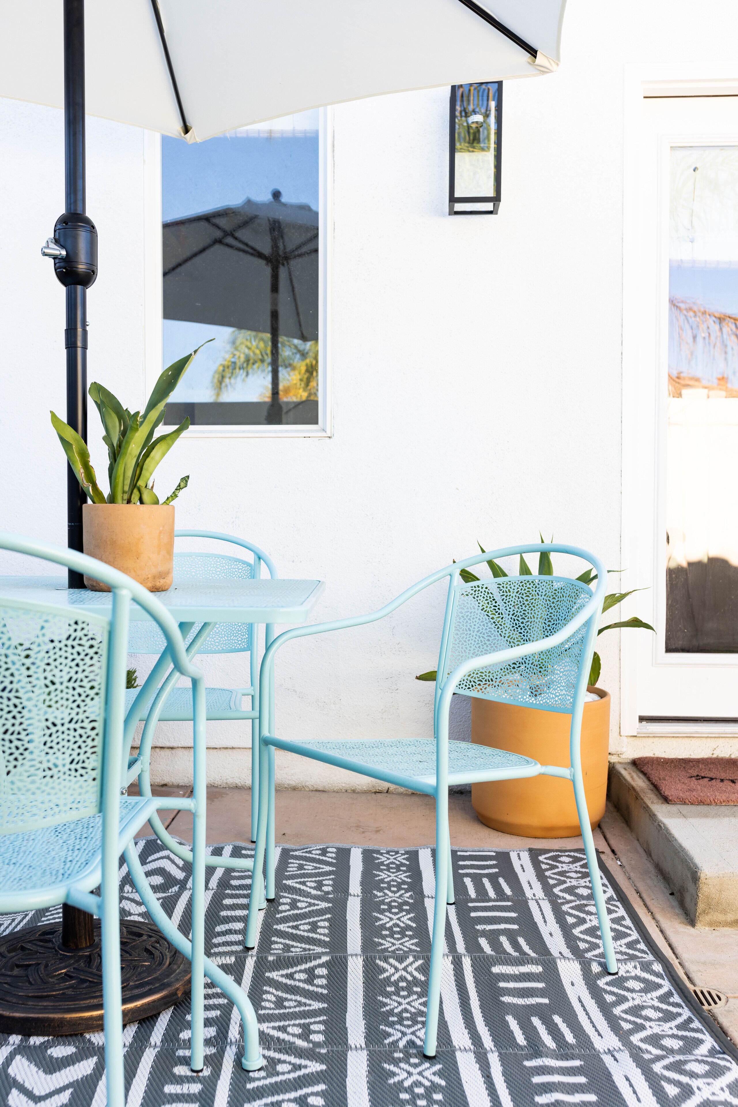 Un espace patio aménagé avec une table et des chaises, une plante en pot et un tapis à motifs.