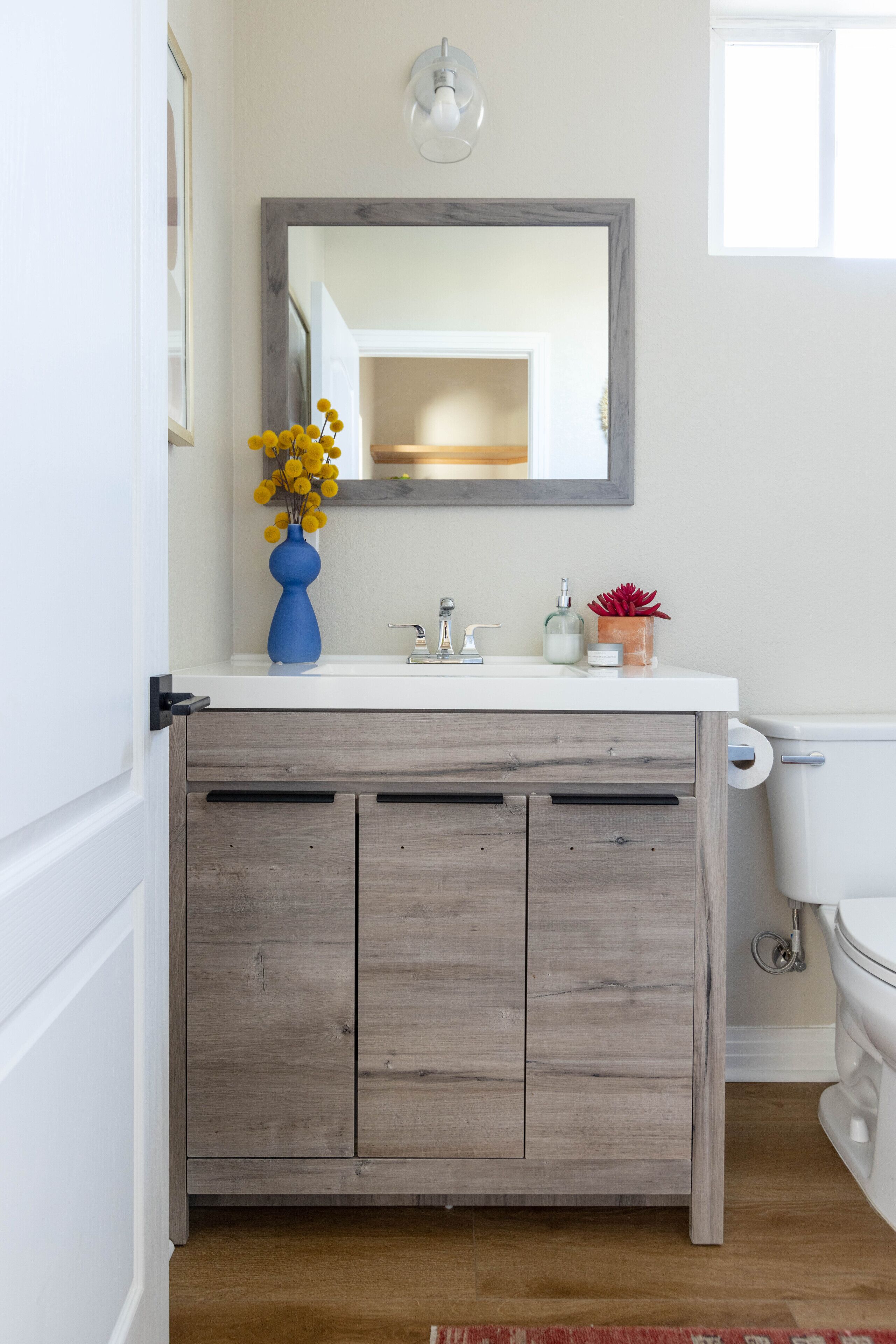 A bathroom with a white sink, wooden cabinet, and a mirror above it.
