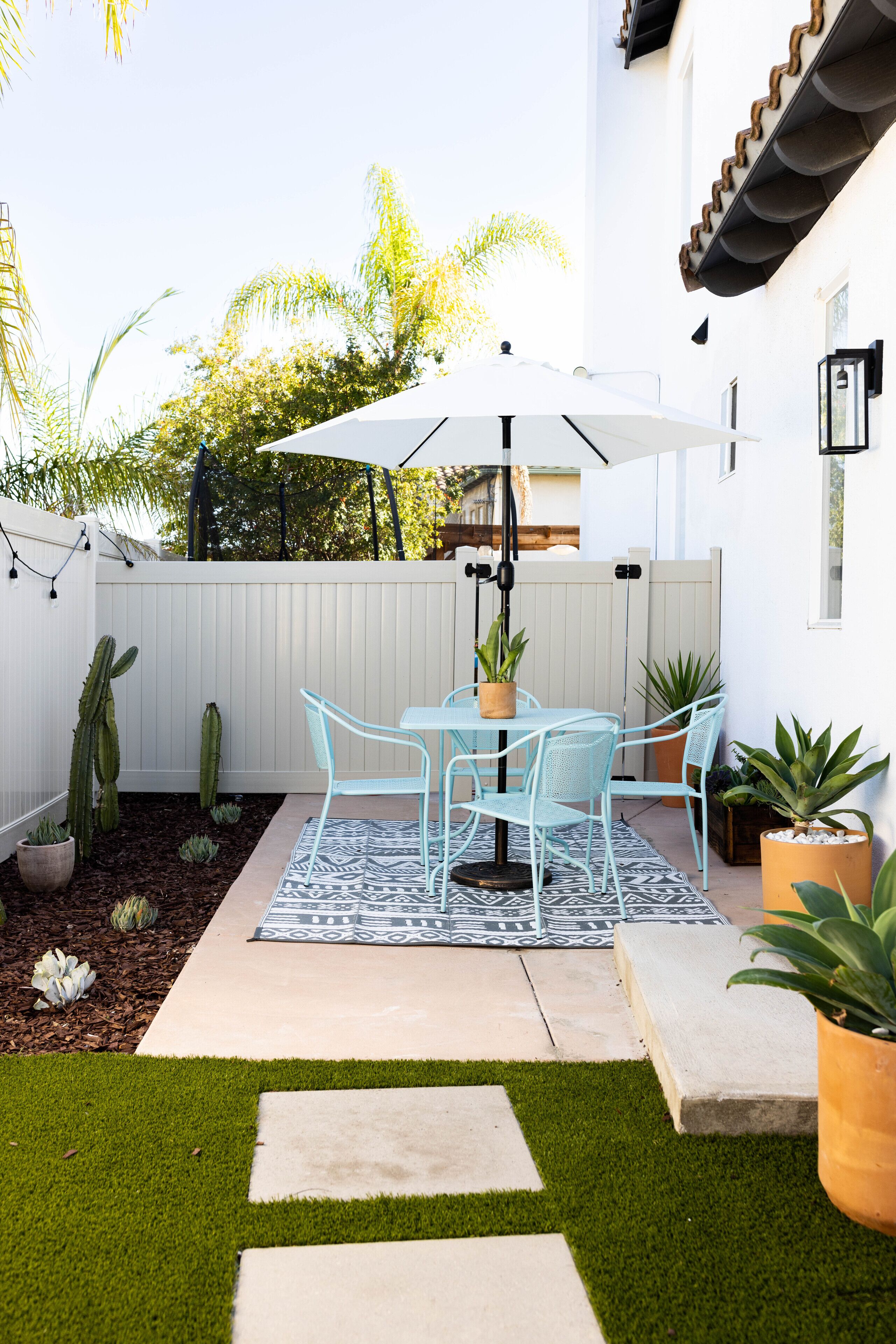 Une terrasse avec une table et des chaises, une clôture blanche et des plantes en pot.
