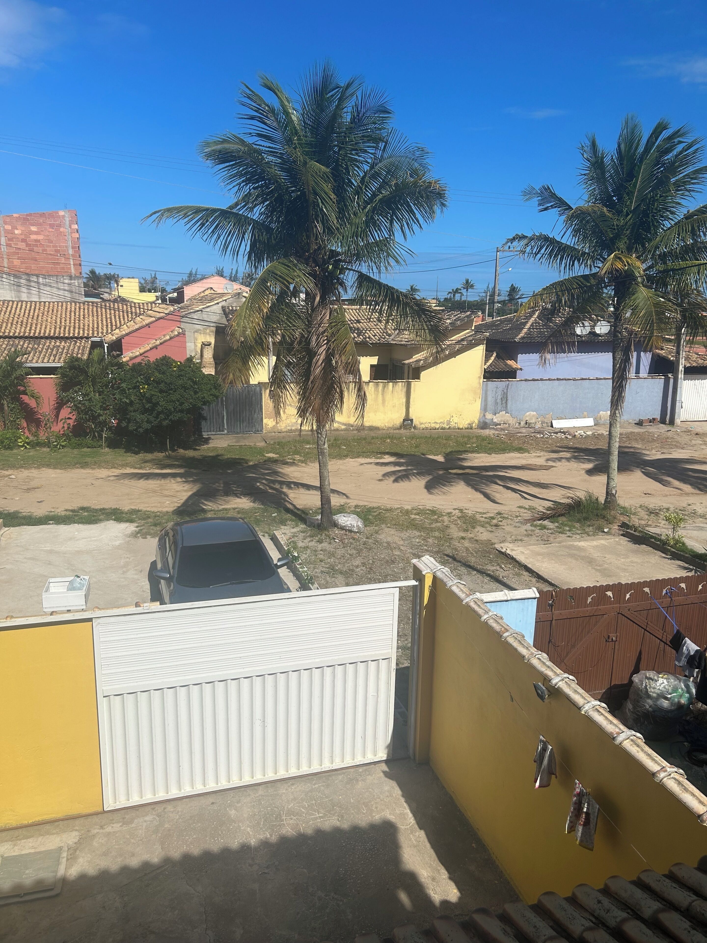 A residential area with a parked car, palm trees, and houses with tiled roofs.