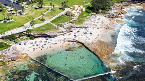 An aerial view of a coastal area with a beach, clear water, and rocky terrain. - 6 bedrooms, ocean views, pool & spa (Cronulla)