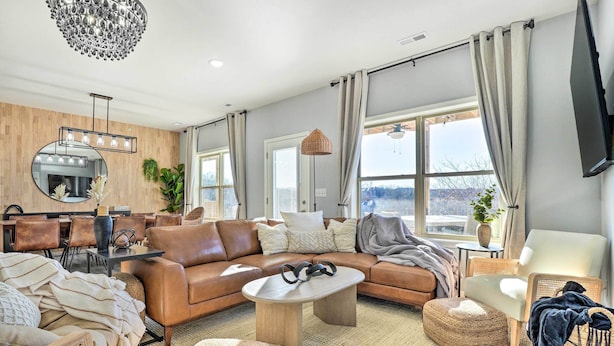 A modern living room with a brown leather sofa, a round coffee table, and a large mirror with lights. - Reeds Spring Condo ~ 3 Mi to Silver Dollar City! (Reeds Spring)