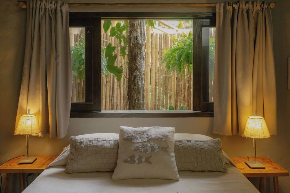 A bed with two pillows, a window with curtains, and two bedside lamps.