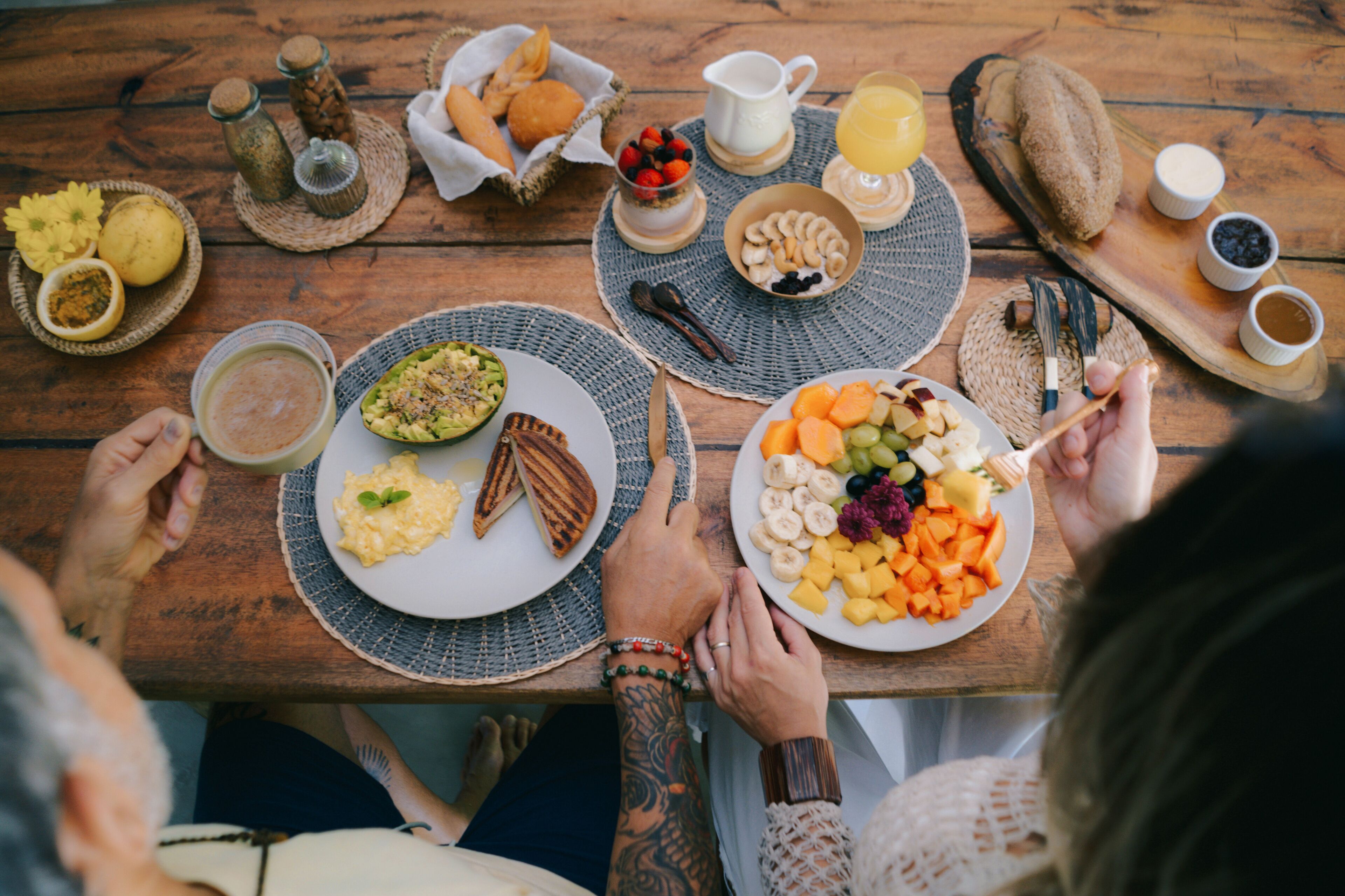 Une table en bois sur laquelle sont disposés divers aliments pour le petit-déjeuner, notamment des œufs, des toasts, des fruits et des viennoiseries.